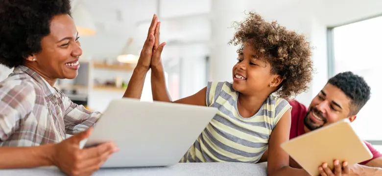 Menyw yn dal gliniadur ac yn rhoi high five i blentyn